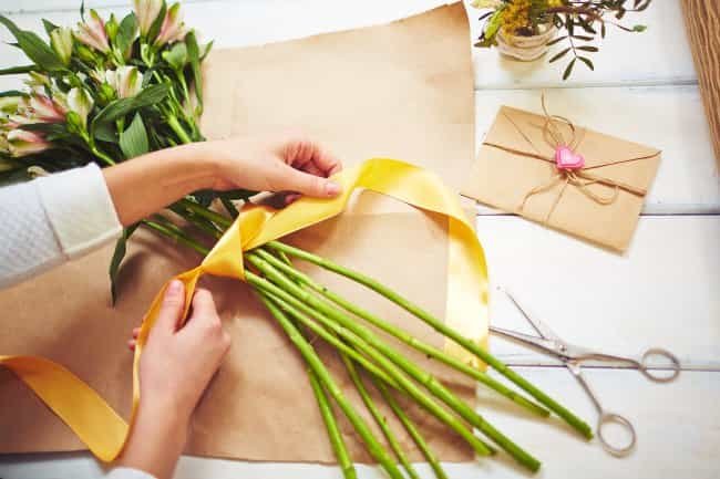 Female Florist Tying Up Fresh Flowers With Silk Ribbon